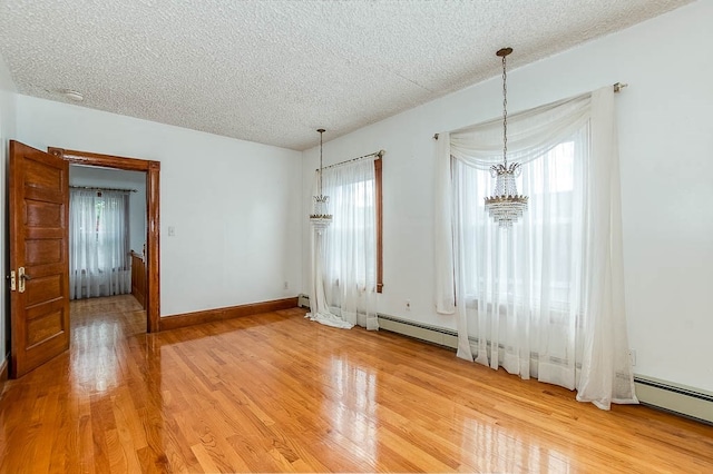 empty room featuring light hardwood / wood-style flooring, a chandelier, a textured ceiling, and a baseboard heating unit