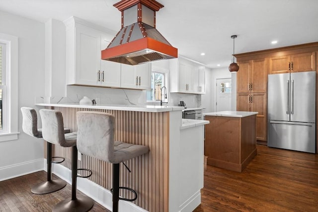 kitchen with white cabinetry, high end refrigerator, a breakfast bar, and island range hood