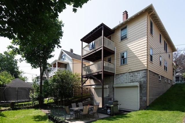 105 Fletcher St Unit 1, Boston, MA 02131 - rear view of house featuring a trampoline, a balcony, a lawn, a chimney, and a patio