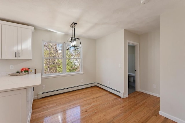 unfurnished dining area with light wood-type flooring, baseboards, a notable chandelier, and a baseboard radiator