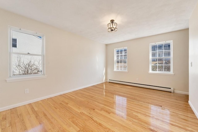 empty room featuring a baseboard heating unit, wood finished floors, and baseboards