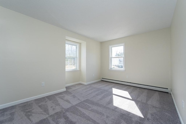 carpeted spare room with a baseboard heating unit, plenty of natural light, and baseboards