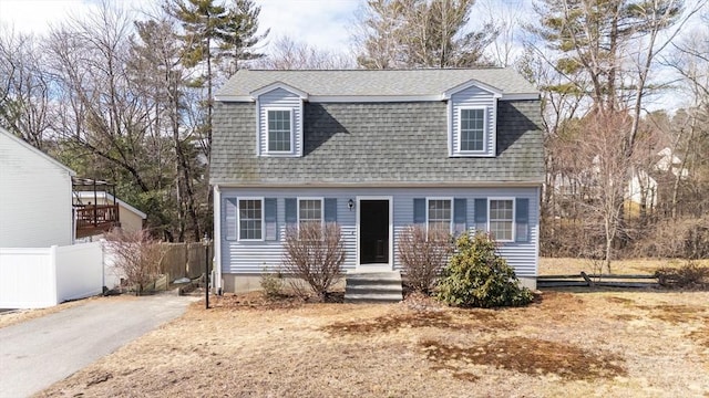 dutch colonial featuring fence, driveway, and a shingled roof