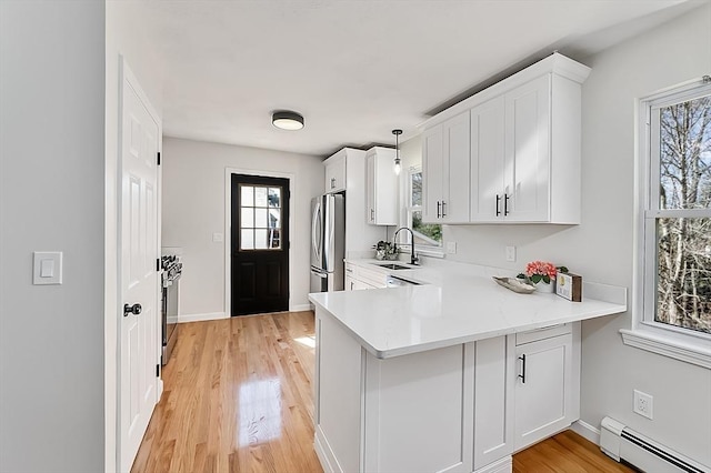 kitchen featuring baseboard heating, white cabinets, freestanding refrigerator, and a sink