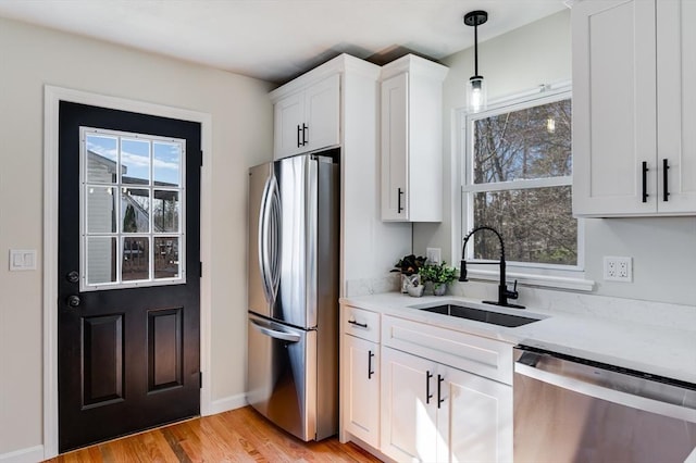 kitchen with a sink, appliances with stainless steel finishes, white cabinets, light wood finished floors, and light stone countertops