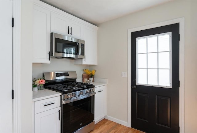 kitchen featuring light stone counters, baseboards, stainless steel appliances, white cabinetry, and light wood-type flooring