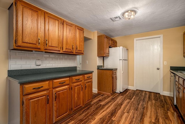 kitchen with dark wood finished floors, dark countertops, brown cabinetry, and visible vents