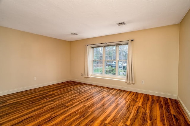 spare room featuring wood finished floors, visible vents, and baseboards