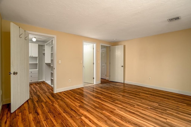 unfurnished bedroom with a walk in closet, baseboards, wood finished floors, and visible vents