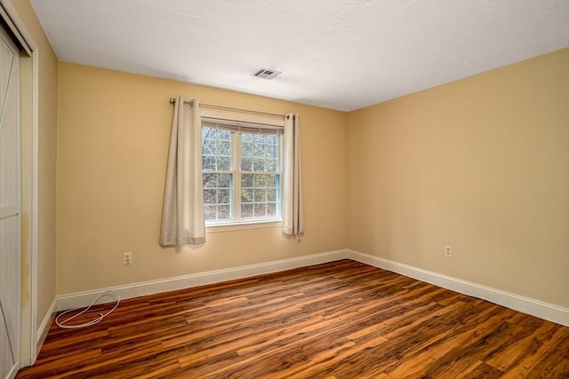 empty room with wood finished floors, visible vents, and baseboards