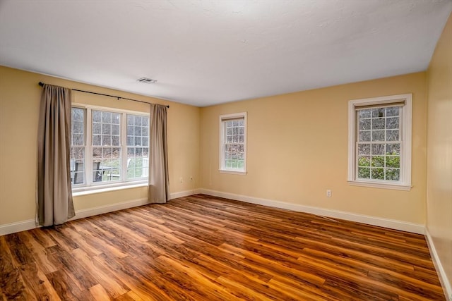 spare room featuring baseboards, wood finished floors, visible vents, and a wealth of natural light