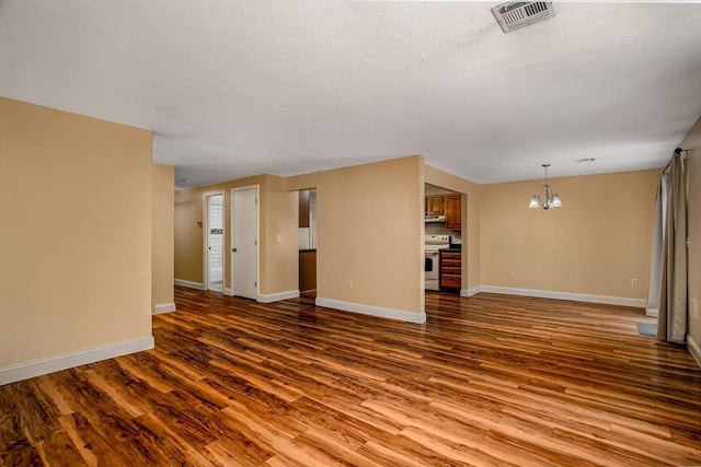 unfurnished living room featuring wood finished floors, visible vents, baseboards, and an inviting chandelier