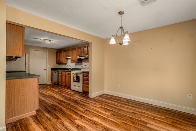 kitchen featuring under cabinet range hood, dark countertops, white appliances, dark wood-type flooring, and baseboards