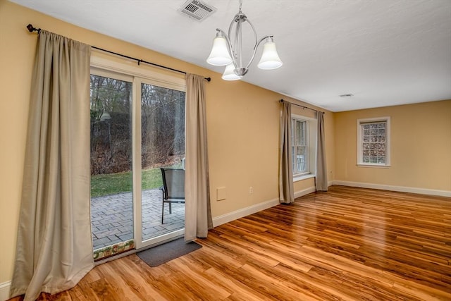 interior space featuring baseboards, wood finished floors, visible vents, and an inviting chandelier