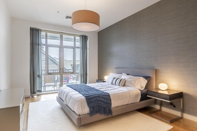 bedroom featuring an accent wall, wood finished floors, wallpapered walls, and baseboards