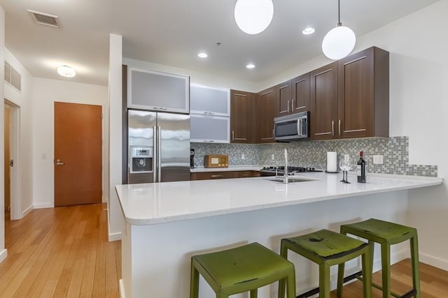 kitchen featuring stainless steel appliances, a peninsula, dark brown cabinetry, backsplash, and light wood finished floors