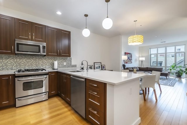 kitchen with stainless steel appliances, a peninsula, open floor plan, light wood-style flooring, and recessed lighting