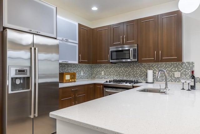 kitchen with appliances with stainless steel finishes, a sink, light stone countertops, backsplash, and dark brown cabinetry
