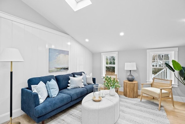 living room featuring vaulted ceiling with skylight, a healthy amount of sunlight, and light hardwood / wood-style flooring