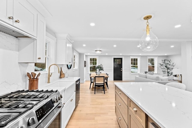 kitchen with appliances with stainless steel finishes, decorative light fixtures, light stone counters, and light hardwood / wood-style flooring