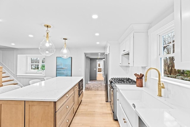 kitchen featuring white cabinetry, stainless steel appliances, light stone counters, a kitchen island, and light wood-type flooring