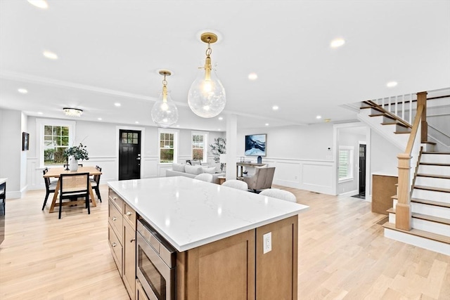 kitchen featuring pendant lighting, light hardwood / wood-style flooring, stainless steel microwave, and a healthy amount of sunlight