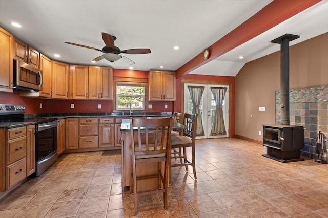 40 George St, Attleboro, MA 02703 - kitchen featuring stainless steel appliances, a ceiling fan, a wood stove, a kitchen bar, and dark countertops