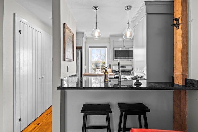 kitchen with stainless steel appliances, hardwood / wood-style floors, hanging light fixtures, a breakfast bar area, and dark stone countertops