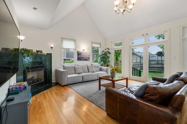 living area featuring an inviting chandelier, a fireplace, high vaulted ceiling, and wood finished floors