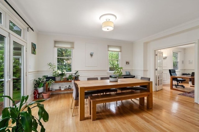 dining area with light wood finished floors, ornamental molding, and a decorative wall