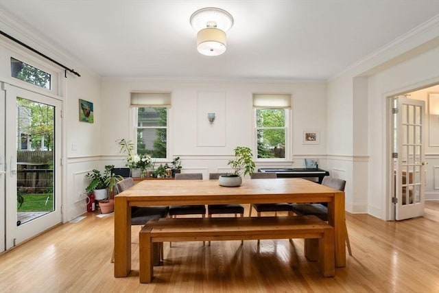 dining area featuring light wood-type flooring, plenty of natural light, a decorative wall, and crown molding