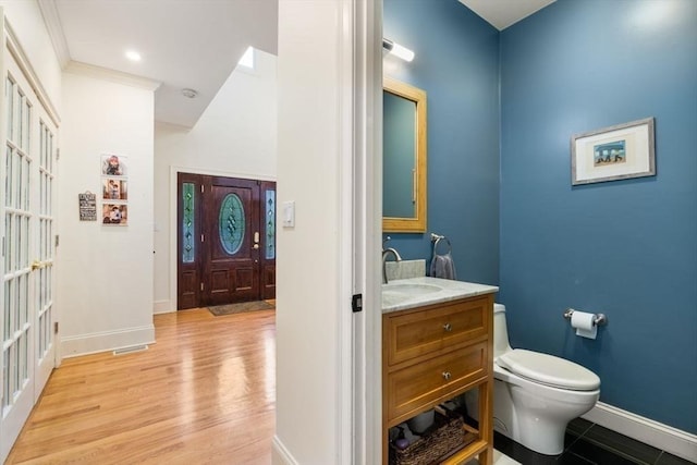 half bath with crown molding, visible vents, toilet, wood finished floors, and baseboards