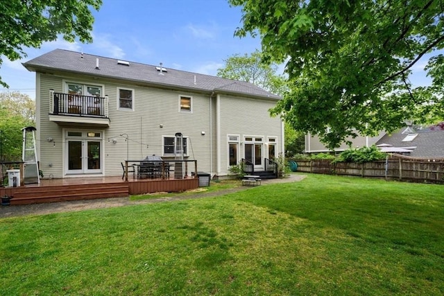 rear view of property featuring a balcony, fence, french doors, and a yard