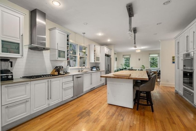 kitchen featuring a sink, wooden counters, appliances with stainless steel finishes, a center island, and wall chimney exhaust hood