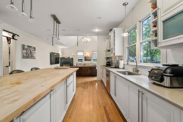 kitchen with butcher block countertops, a sink, white cabinetry, dishwasher, and tasteful backsplash