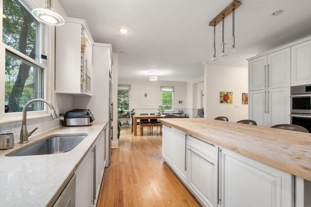 kitchen with tasteful backsplash, light wood-style floors, stainless steel double oven, a sink, and wood counters