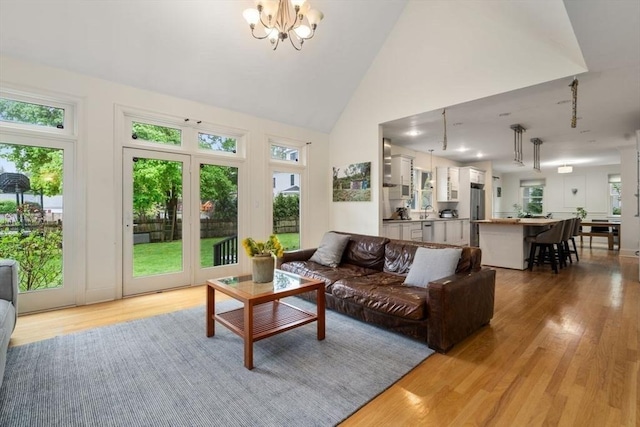 living room with a healthy amount of sunlight, light wood-style floors, high vaulted ceiling, and a notable chandelier