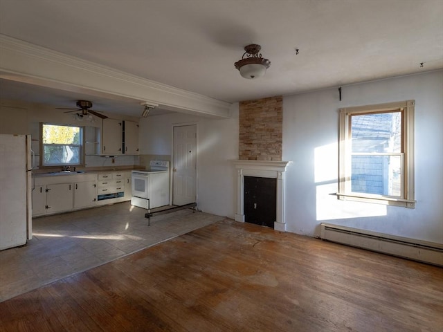 unfurnished living room with ceiling fan, sink, a stone fireplace, light hardwood / wood-style flooring, and a baseboard heating unit