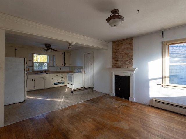 unfurnished living room with sink, ceiling fan, a fireplace, a baseboard radiator, and wood-type flooring