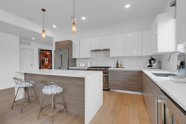 kitchen featuring pendant lighting, sink, white cabinets, high end appliances, and light hardwood / wood-style flooring