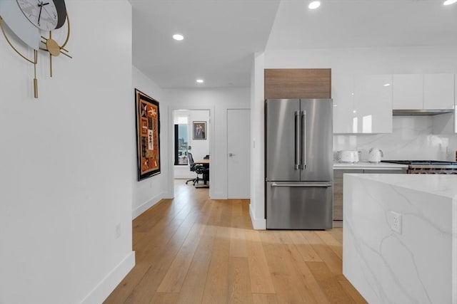 kitchen with white cabinets, backsplash, light stone countertops, high end fridge, and light hardwood / wood-style flooring