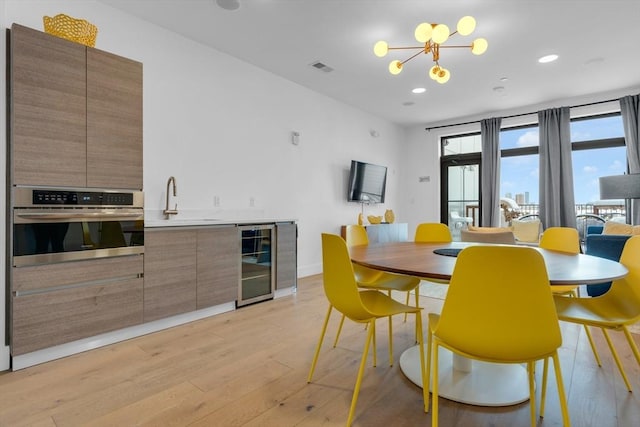 dining room with sink, beverage cooler, a chandelier, and light wood-type flooring