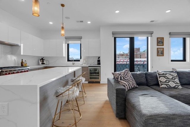 kitchen with wine cooler, decorative light fixtures, light wood-type flooring, decorative backsplash, and white cabinets