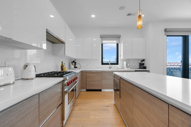 kitchen featuring wall chimney range hood, decorative light fixtures, high end stove, and white cabinets