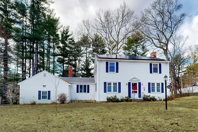 colonial-style house featuring a front yard, roof mounted solar panels, and a chimney