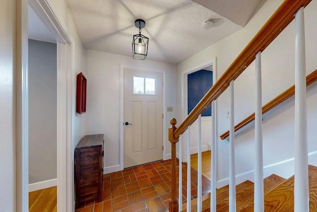 foyer featuring brick floor, baseboards, and stairs