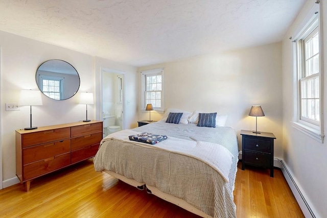 bedroom featuring light wood-style flooring, baseboards, ensuite bathroom, and a baseboard radiator