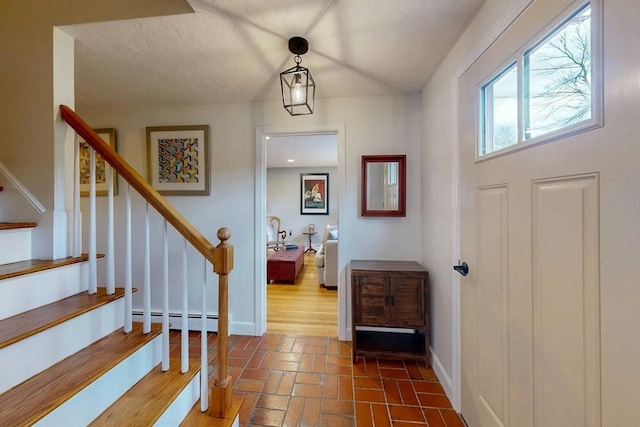 foyer with a baseboard heating unit, stairs, baseboards, and brick floor