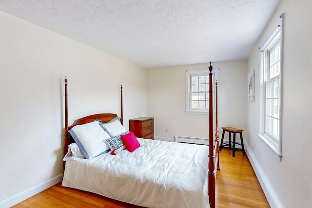 bedroom featuring light wood-type flooring, baseboards, a textured ceiling, and a baseboard radiator