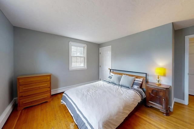 bedroom featuring a baseboard heating unit, wood-type flooring, and baseboards